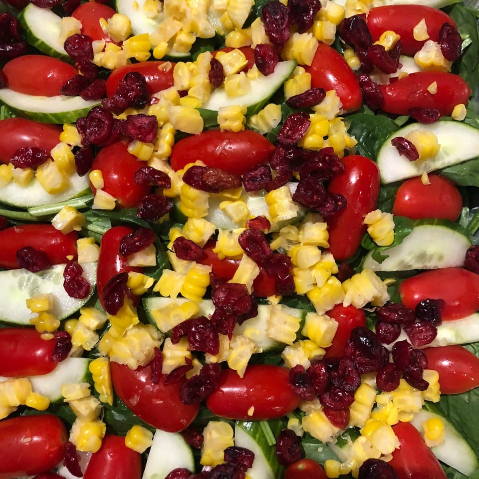 Close-up of a colorful salad with spinach, cucumber, cherry tomatoes, corn, and dried cranberries.