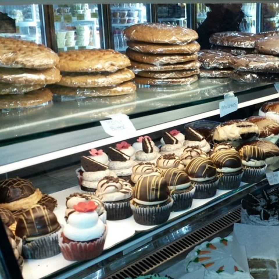 A bakery display case filled with large wrapped cookies and various decorated cupcakes.