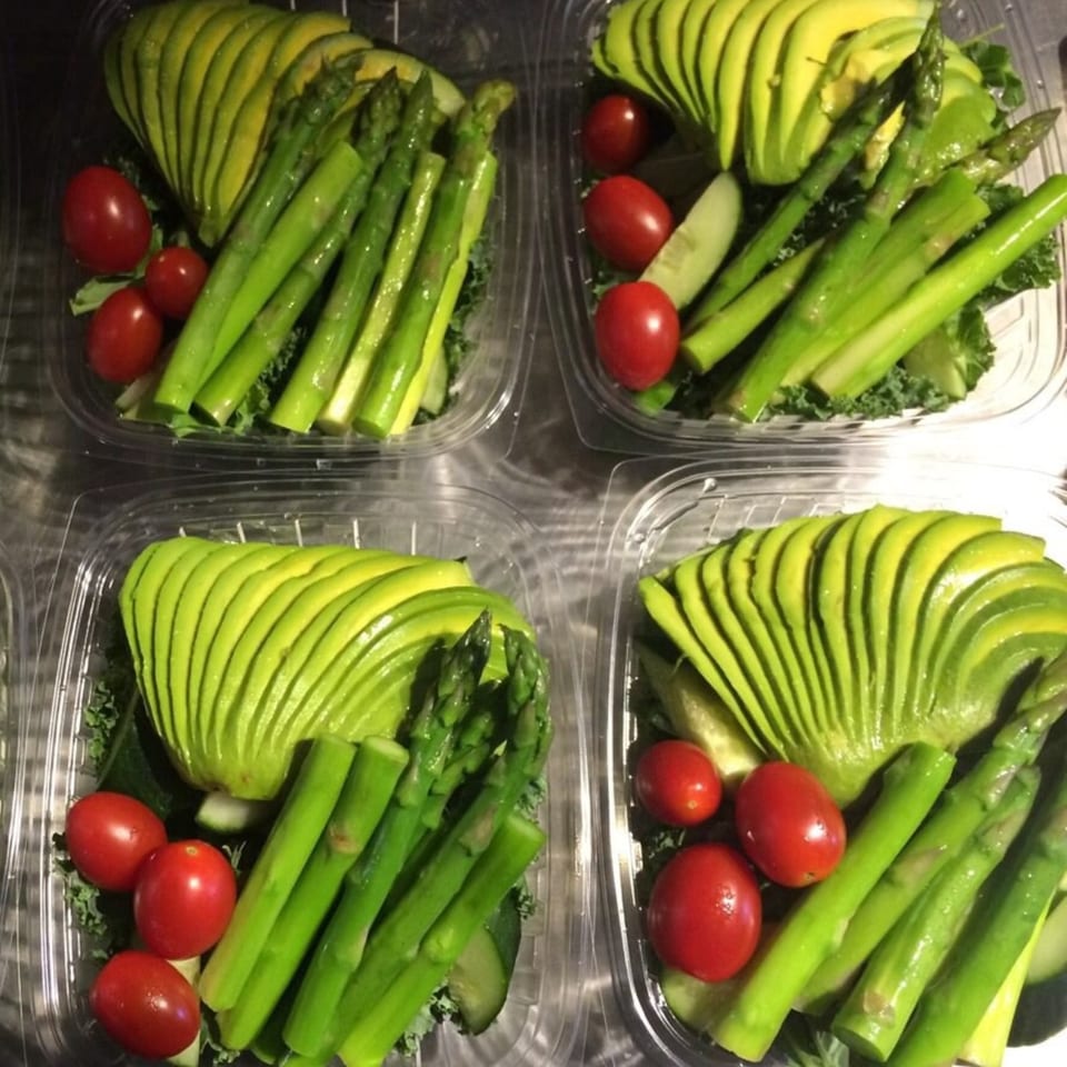 Four clear containers filled with sliced avocado, asparagus, cherry tomatoes, and cucumber.