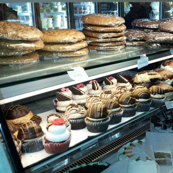 A bakery display case filled with wrapped cookies, various cupcakes, and cakes.