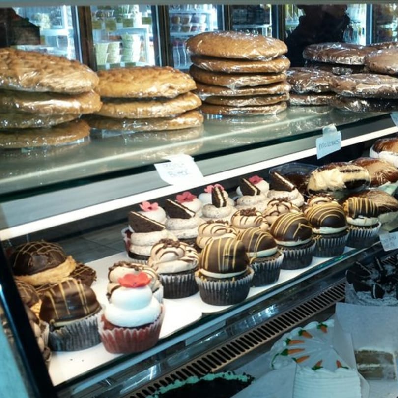 A bakery display case filled with wrapped cookies, various cupcakes, and cakes.