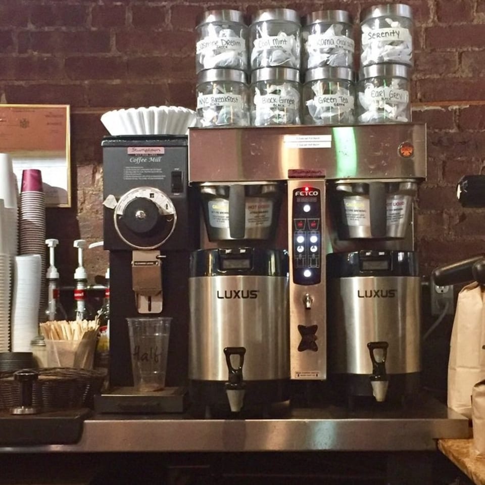 A coffee and tea station with a Stumptown coffee mill, Fetco brewers, and jars of tea.