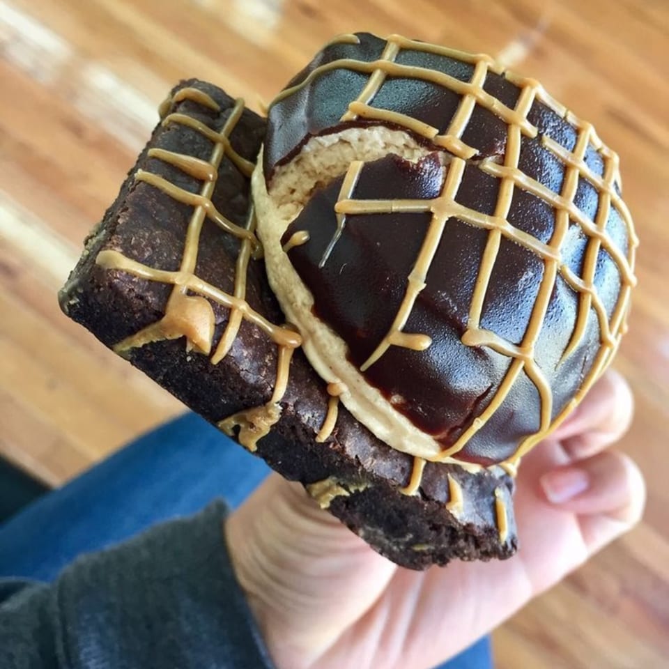 A hand holds a chocolate brownie topped with a peanut butter cup and peanut butter drizzle.