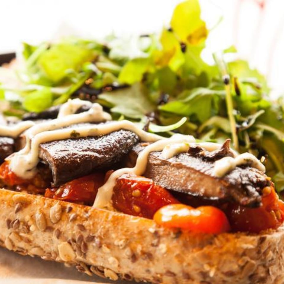 Toasted bread with mushrooms, tomatoes, and a creamy sauce, served with a side salad.